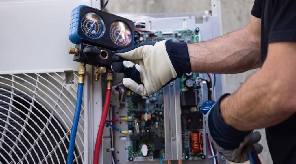 HVAC technician adjusting manifold gauge valves on air conditioner circuit board panel