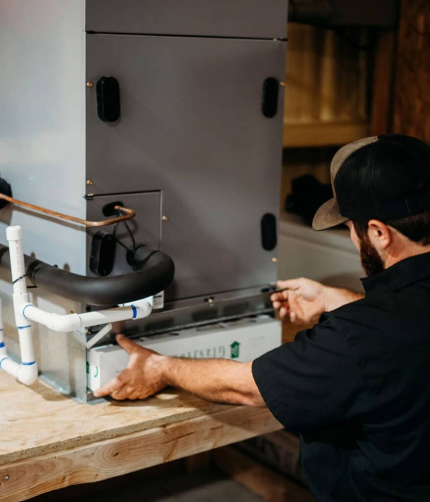 HVAC technician assembling furnace unit with PVC venting on workshop bench