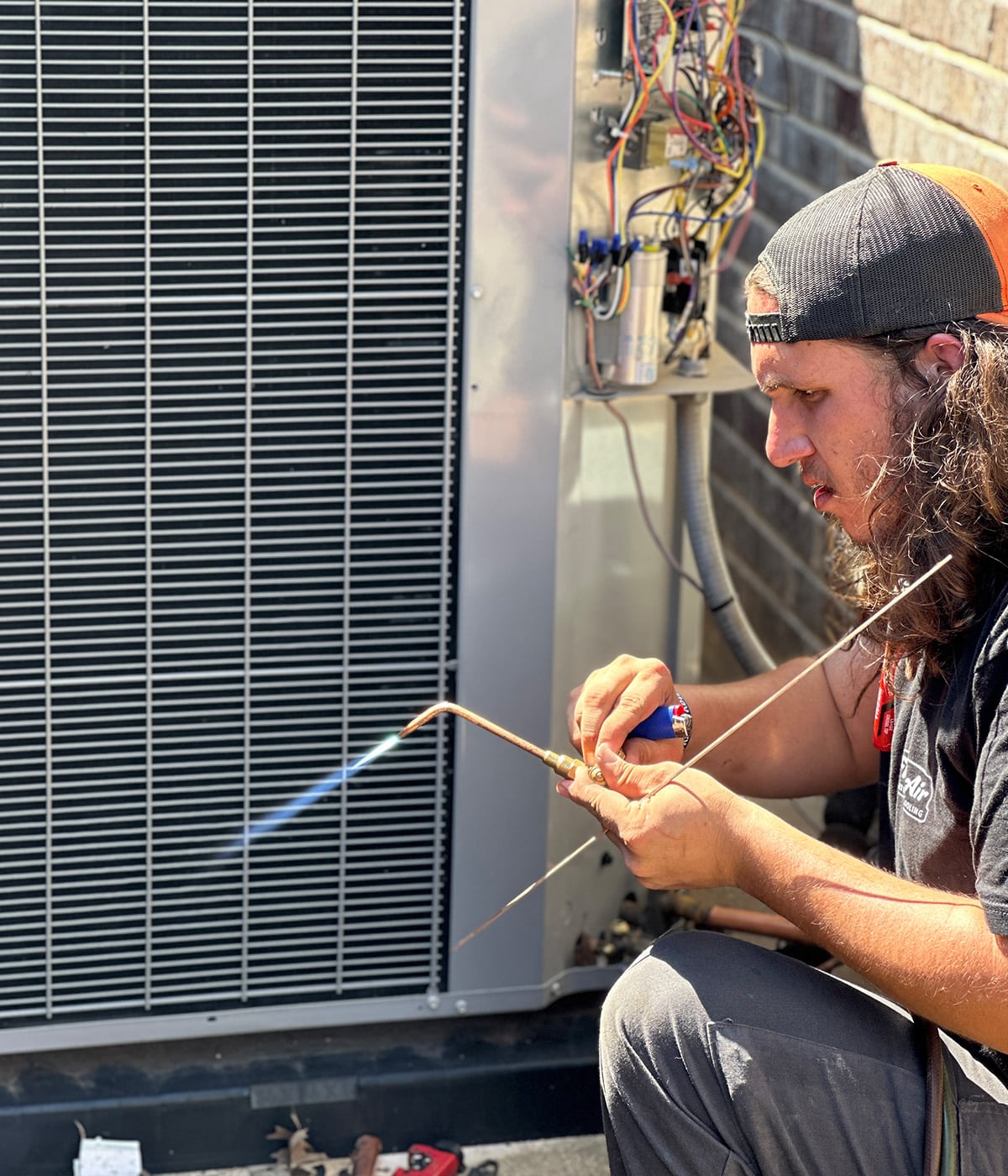 HVAC technician brazing copper refrigerant line with torch on outdoor condenser unit