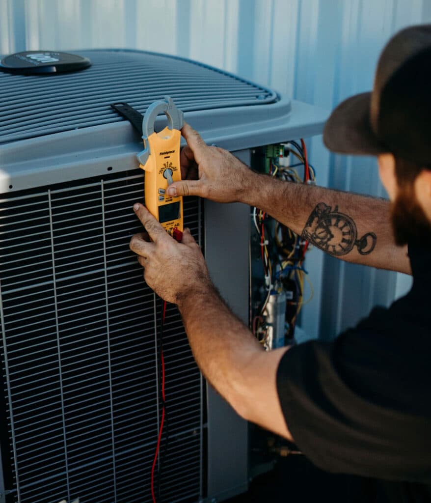 HVAC technician using clamp meter to test condenser unit electrical current