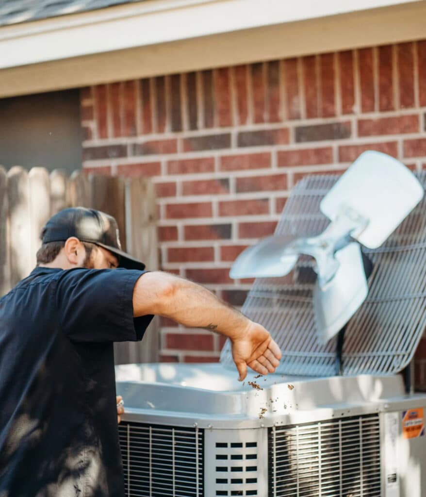 HVAC technician cleaning debris from open condenser unit fan cover