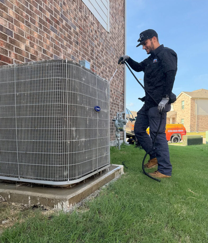 HVAC technician rinsing and cleaning outdoor air conditioner condenser unit coils with hose