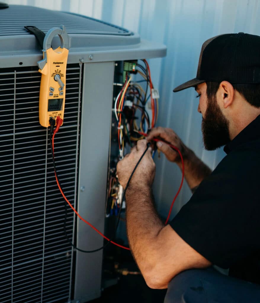 HVAC technician connecting clamp meter wires inside condenser unit control panel