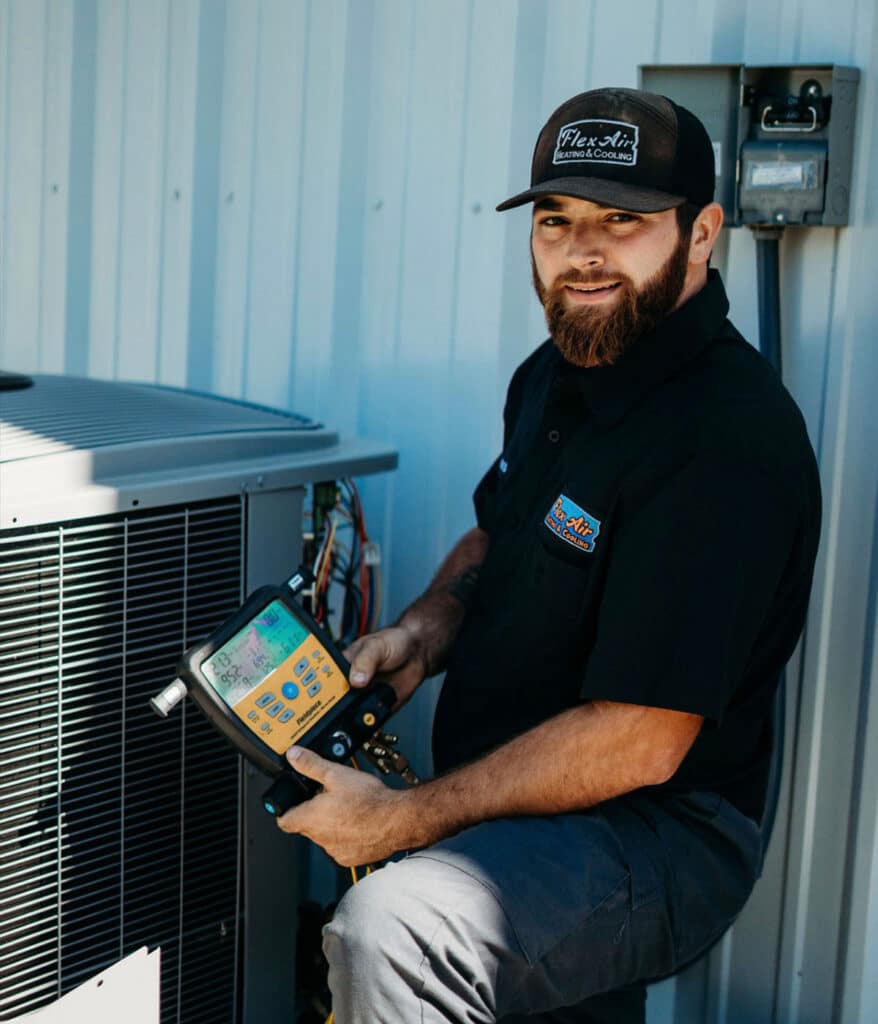 Smiling HVAC technician holding refrigerant gauge tool beside condenser unit