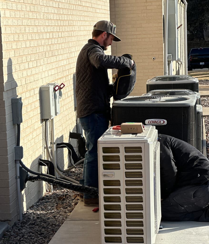 HVAC technician insulating refrigerant line set beside row of condenser units