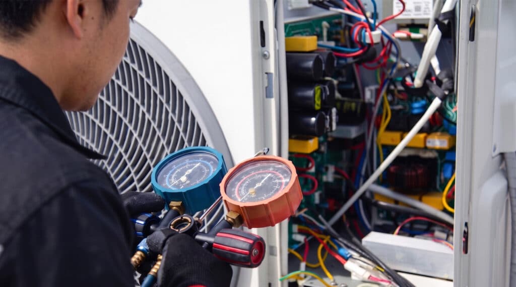 HVAC technician using manifold gauge set to check refrigerant pressure on an air conditioning unit with open electrical panel