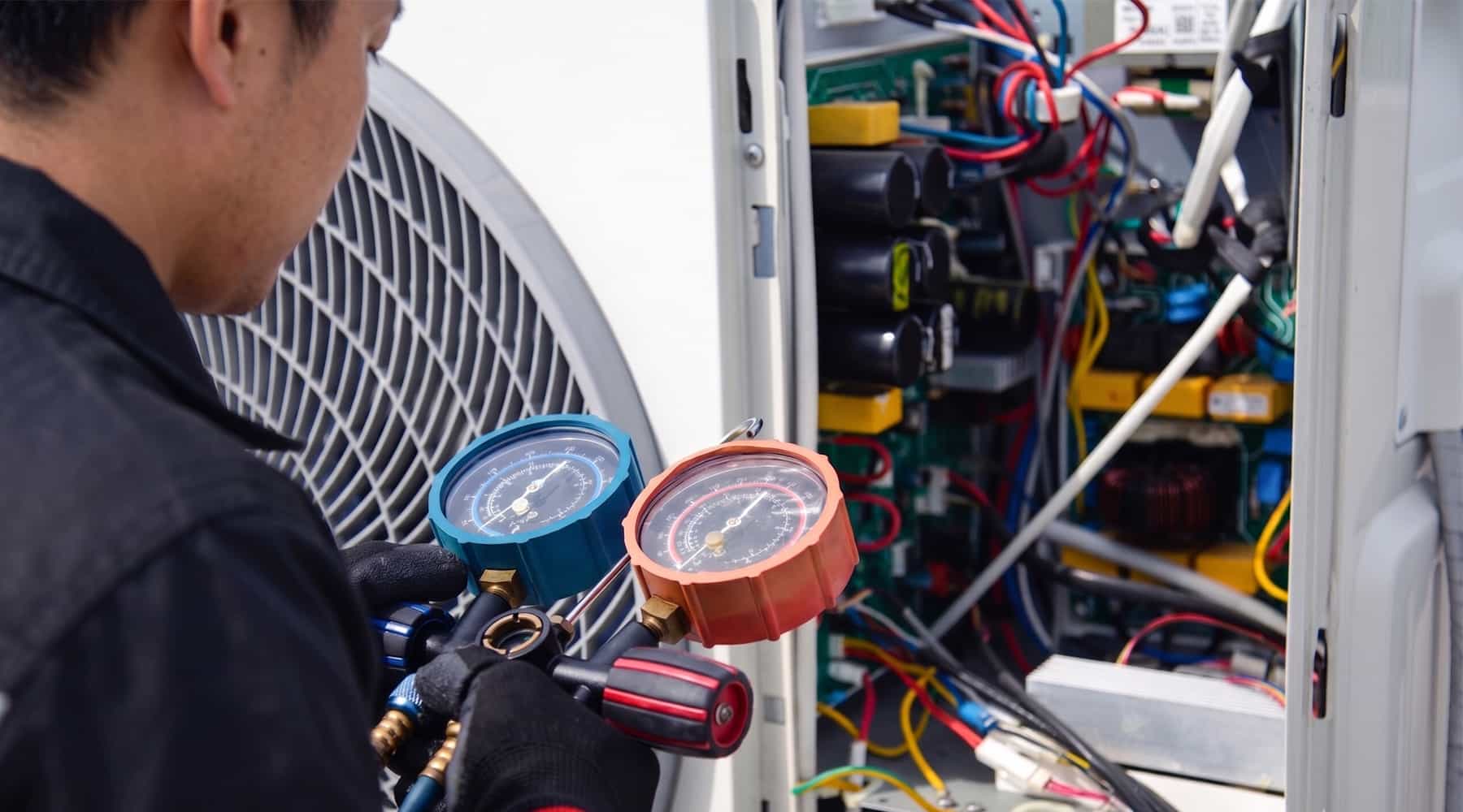 HVAC technician using manifold gauge set to check refrigerant pressure on an air conditioning unit with open electrical panel