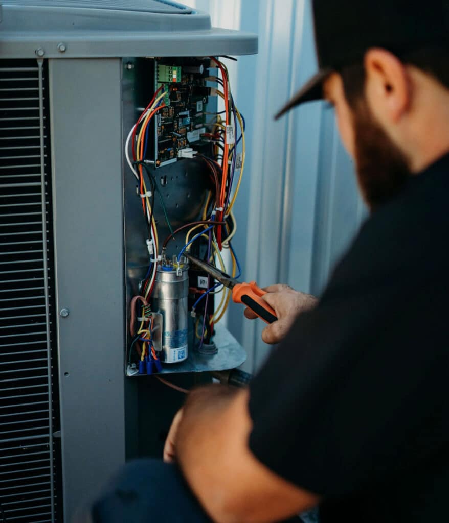 HVAC technician using pliers to repair wiring inside condenser unit electrical panel