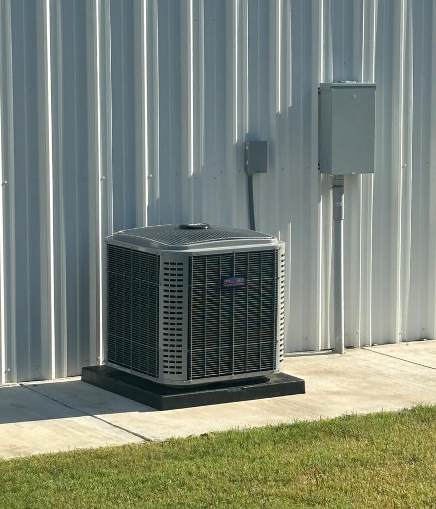 Outdoor air conditioner condenser unit installed beside metal building with electrical panels